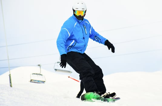close up casual snowboard rider in blue black outfit looks down to camera isolated in white snowy background. Winter vacation with sports mountains photo