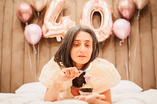 Adult happy beautiful woman forty years with festive cupcake with candle in hands, isolated on white, birthday girl. Natural looking mature woman celebrate happy birthday light up one cupcake candle photo