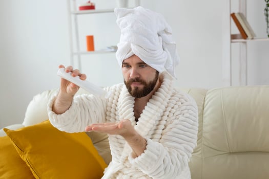 Bearded man holds white bottle cream or gel for skin care. Spa, body and skin care for man concept photo
