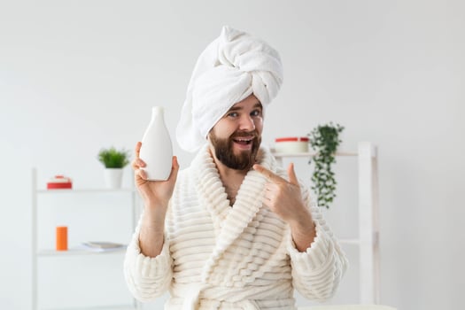 Beauty portrait of handsome beautiful guy in towel and bathrobe holding tube of body cream lotion in hand. Spa, body and skin care for man concept photo