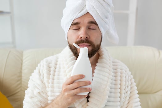 Bearded male with towel on his head applying body lotion cream. Guy smile when smell lotion cream on hand. Spa, body and skin care for man concept photo