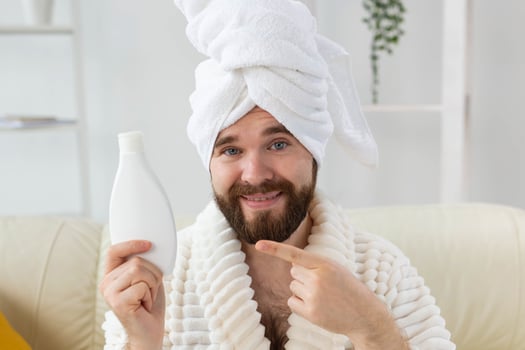 Handsome bearded guy applying moisturizer body cream from container. Spa, body and skin care for man concept. Place for advertisement photo