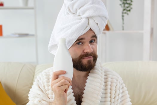 Handsome bearded guy applying moisturizer body cream from container. Spa, body and skin care for man concept. Place for advertisement photo