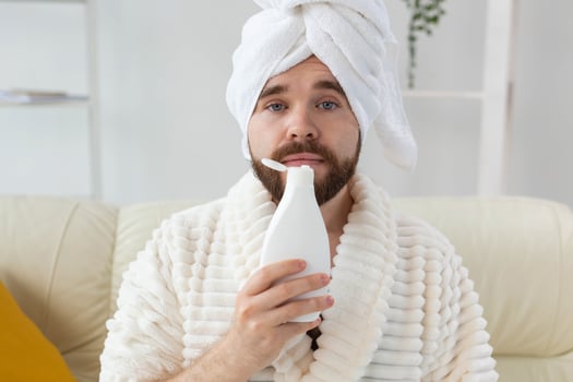 Bearded male with towel on his head applying body lotion cream. Guy smile when smell lotion cream on hand. Spa, body and skin care for man concept photo