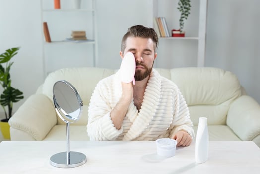 Bearded man look in mirror and clean scrub face with sponge, happy millennial male metrosexual do beauty procedures at home, take care of healthy skin, skincare concept photo
