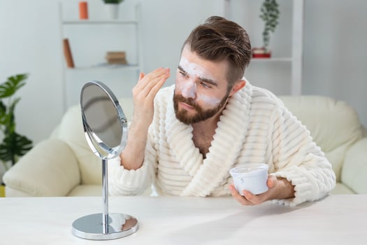 Bearded guy applying facial cream in front of mirror Skin care and spa for man concept. photo
