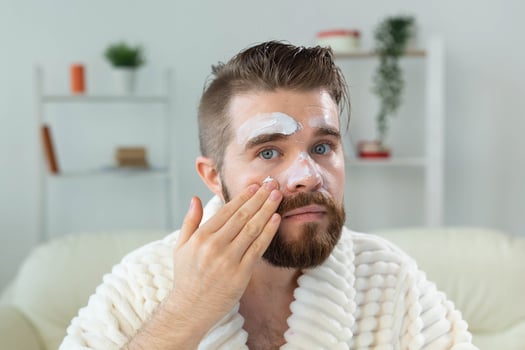 Bearded guy applying facial cream in front of mirror Skin care and spa for man concept. photo