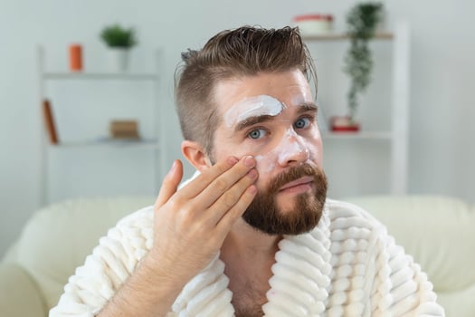 Bearded guy applying anti-wrinkle cream on his face. Skin care and spa for man concept. photo