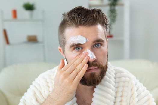 Bearded guy applying anti-wrinkle cream on his face. Skin care and spa for man concept. photo