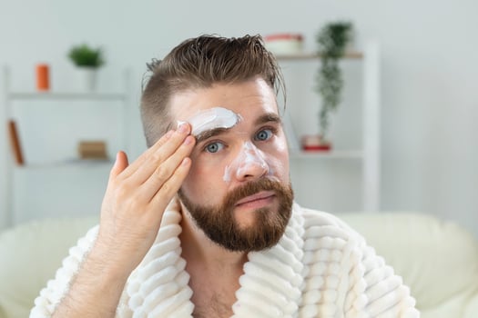 Bearded guy applying facial cream in front of mirror Skin care and spa for man concept. photo