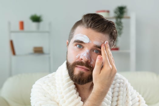 Bearded guy applying anti-wrinkle cream on his face. Skin care and spa for man concept. photo