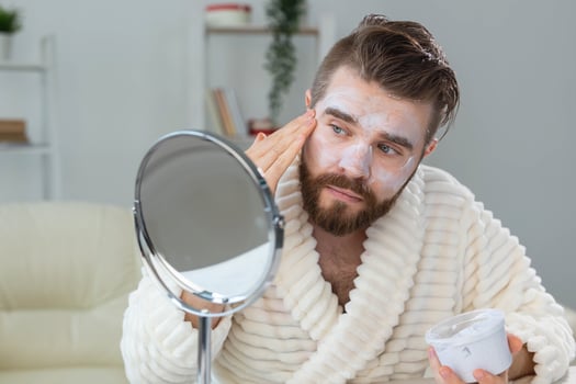 Bearded guy applying facial cream in front of mirror Skin care and spa for man concept. photo