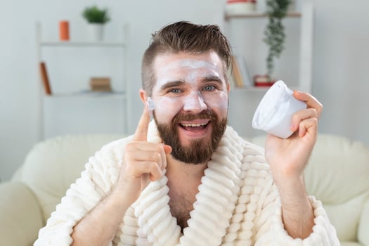 Bearded guy applying facial cream in front of mirror Skin care and spa for man concept. photo