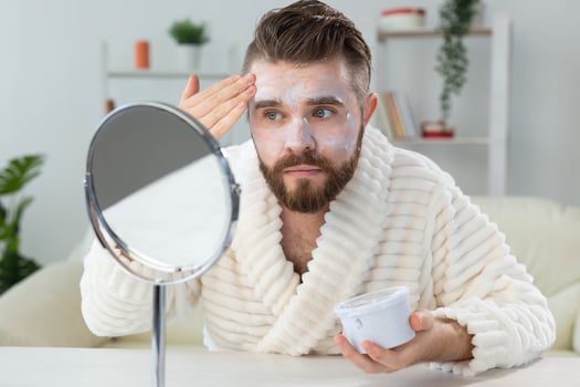 Bearded guy applying facial cream in front of mirror Skin care and spa for man concept. photo