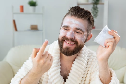 Bearded guy applying facial cream in front of mirror Skin care and spa for man concept. photo