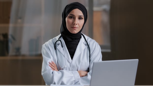 Happy smiling arabian nurse islamic doctor therapist wear white uniform coat hijab sitting at clinic muslim female practitioner intern posing crossed arms looking at camera medical healthcare service photo