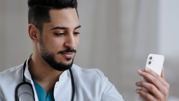 Confident qualified physician male arabian doctor use smartphone social medical app consult clients online in clinic cabinet remote communication give advice telemedicine healthcare services concept photo