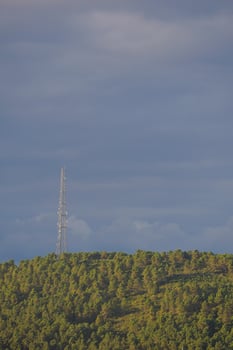 A Telecommunication Tower Standing Tall on a Lush Green Hill Beneath a Dramatic Sky Full of Clouds photo
