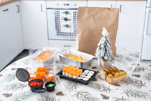 Delivery of sushi and rolls in food containers on the table in the festive interior of the kitchen of the house with a white Christmas tree for Christmas and New year. Food delivery for the holidays photo