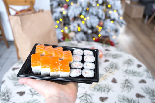 Delivery of sushi and rolls set is hold in hand in the festive interior of house with a white Christmas tree for Christmas and New year. Food delivery for the holidays photo