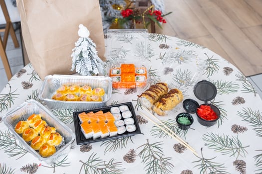Delivery of sushi and rolls in food containers on the table in the festive interior of the kitchen of the house with a white Christmas tree for Christmas and New year. Food delivery for the holidays photo