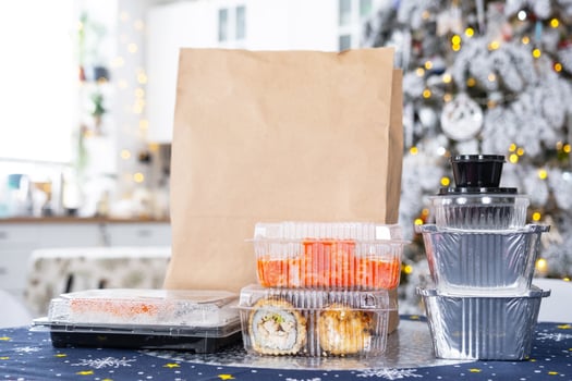 Delivery of sushi and rolls in food containers on the table in the festive interior of the kitchen of the house with a white Christmas tree for Christmas and New year. Food delivery for the holidays photo