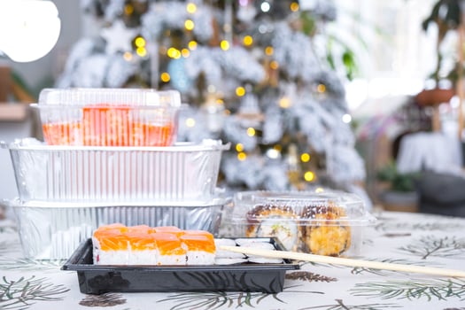 Delivery of sushi and rolls in food containers on the table in the festive interior of the kitchen of the house with a white Christmas tree for Christmas and New year. Food delivery for the holidays photo
