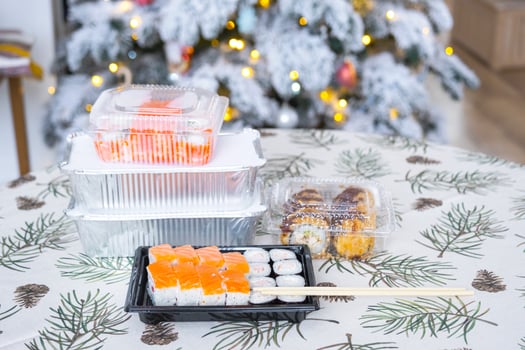 Delivery of sushi and rolls in food containers on the table in the festive interior of the kitchen of the house with a white Christmas tree for Christmas and New year. Food delivery for the holidays photo