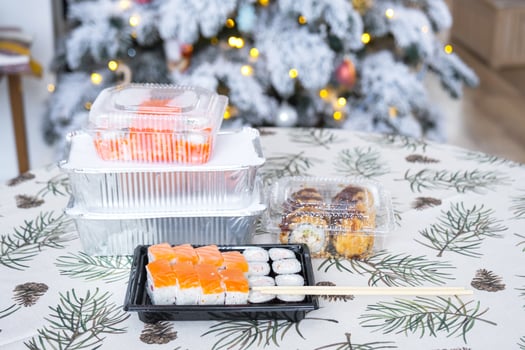 Delivery of sushi and rolls in food containers on the table in the festive interior of the kitchen of the house with a white Christmas tree for Christmas and New year. Food delivery for the holidays photo