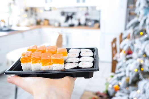 Delivery of sushi and rolls set is hold in hand in the festive interior of house with a white Christmas tree for Christmas and New year. Food delivery for the holidays photo