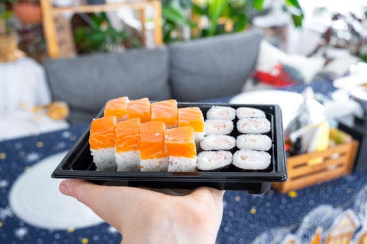 Delivery of sushi and rolls set is hold in hand in the festive interior of house with a white Christmas tree for Christmas and New year. Food delivery for the holidays photo