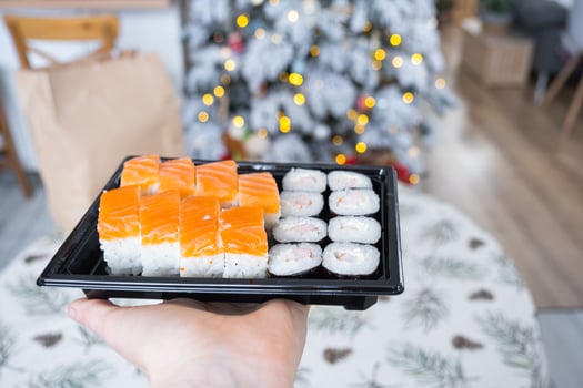 Delivery of sushi and rolls set is hold in hand in the festive interior of house with a white Christmas tree for Christmas and New year. Food delivery for the holidays photo