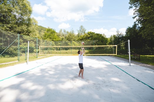 Young man tossing a volleyball into the air on a sandy court during a sunny day. The casual outdoor scene highlights fun, summer sports, and recreation in a natural setting photo
