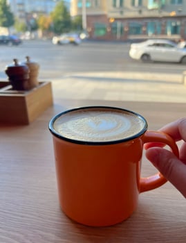 Orange stylish ceramic cup of cappuccino or latte decorated with foam on overlooking the street and the road and moving cars. Morning coffee. Warm Coffee Moment in a Cozy Caf Setting photo