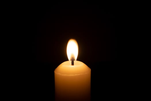 A single burning candle flame or light glowing on a big white candle isolated on red or dark background on table in church for Christmas, funeral or memorial service photo