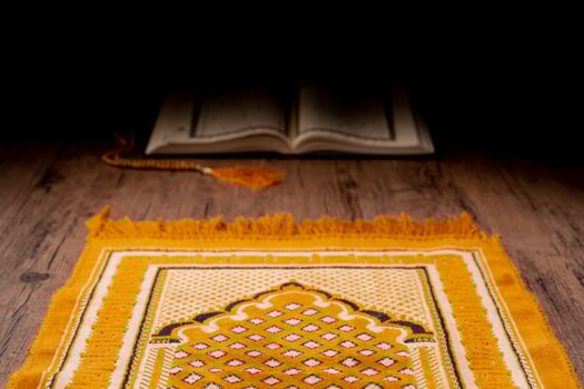 A Asian Muslim woman is sitting and reading the Quran at the wooden table at his house during the night during the month of ramadan, Arabic calligraphy meaning of Al Quran. photo