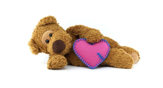 Cute teddy bear holding a pink heart with delicate blue stitching isolated on white background photo