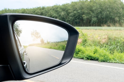 Inside view of mirrors wing. Rear view of a black car with asphalt road and green grass in the daytime. Clear traffic in rural areas. photo