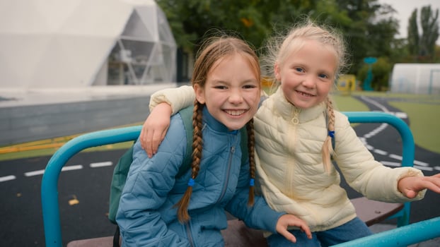 Two little girls friends sisters riding swing laughing smiling joy happiness childhood playground hug fun schoolgirls walk play outside city children classmates kids together school education learning photo