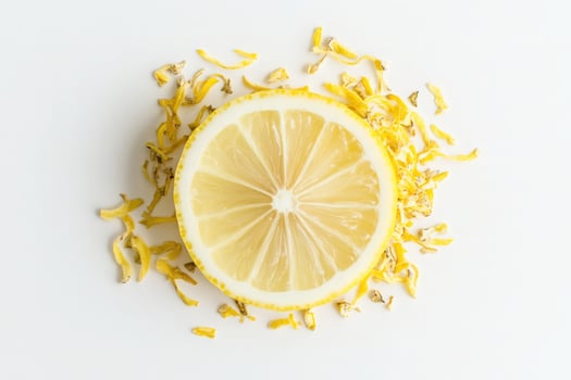 A halved lemon sits at the center, surrounded by vibrant lemon zest that adds texture and brightness. The arrangement highlights the rich color and freshness of the citrus fruit. photo