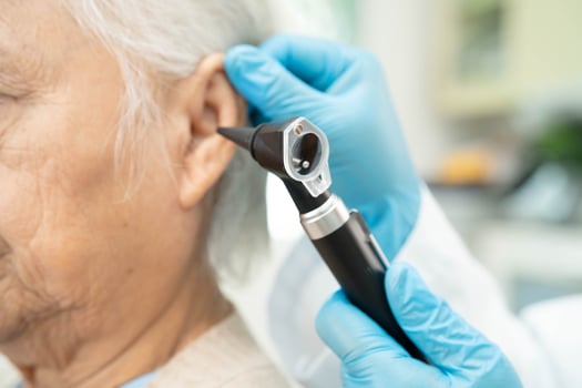 Otolaryngologist or ENT physician doctor examining senior patient ear with otoscope, hearing loss problem. photo