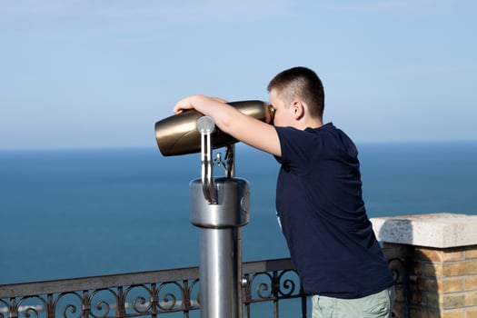 Teenager boy looking in binoculars telescope on observation deck for tourist. Travel, tourism, outdoors lifestyle holiday vacation. Side view photo