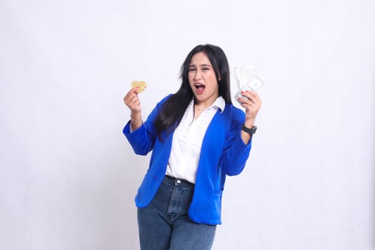 Elegant adult office woman wearing blue formal suit standing cheerful happy to camera hand holding dollar money and bitcoin isolated white background. for transaction content, investment, business photo
