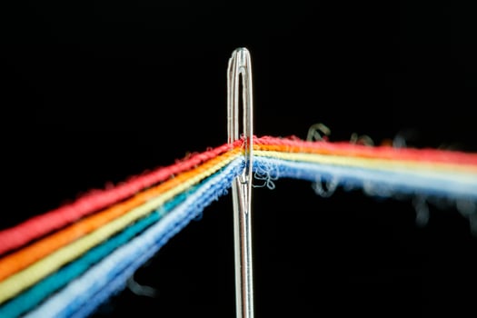multi-colored threads for sewing in the form of a rainbow pass through an antique needle on a black background photo