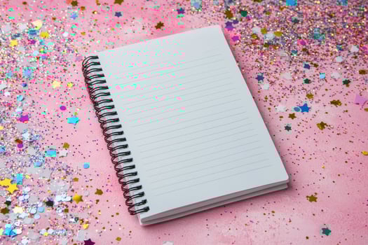 Blank notebook on pink background surrounded by colorful star confetti photo