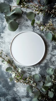 A simple round white plate surrounded by fresh greenery and delicate flowers on a textured surface photo