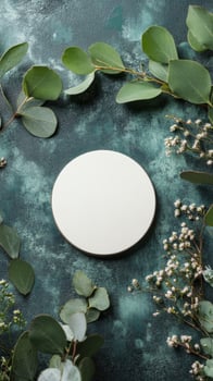 A simple round white plate surrounded by fresh greenery and delicate flowers on a textured surface photo