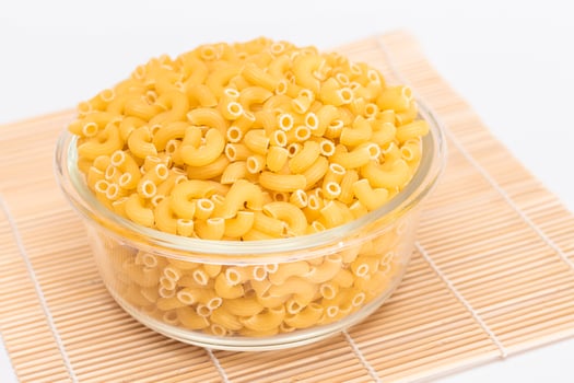 Uncooked Chifferi Rigati Pasta in Glass Jar on Bamboo Mat on White Background. Fat and Unhealthy Food. Classic Dry Macaroni. Italian Culture and Cuisine. Raw Pasta photo