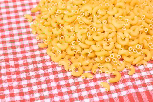 Scattered Uncooked Chifferi Rigati Pasta on Red Checkered Towel. Fat and Unhealthy Food. A Heap of Classic Dry Macaroni. Italian Culture and Cuisine. Raw Pasta photo
