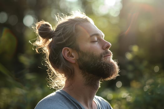 A man with a beard and long hair is sitting in the sun, looking up at the sky photo